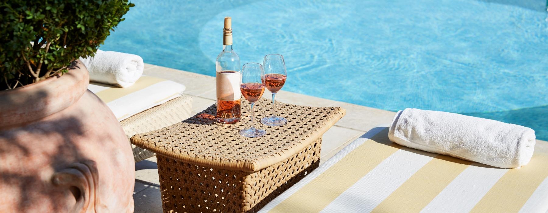 a lounge chair with a table and wine glasses by a pool